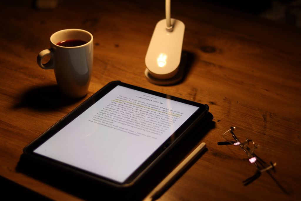 A tablet with a document, coffee, and glasses on a wooden desk in warm evening lighting.