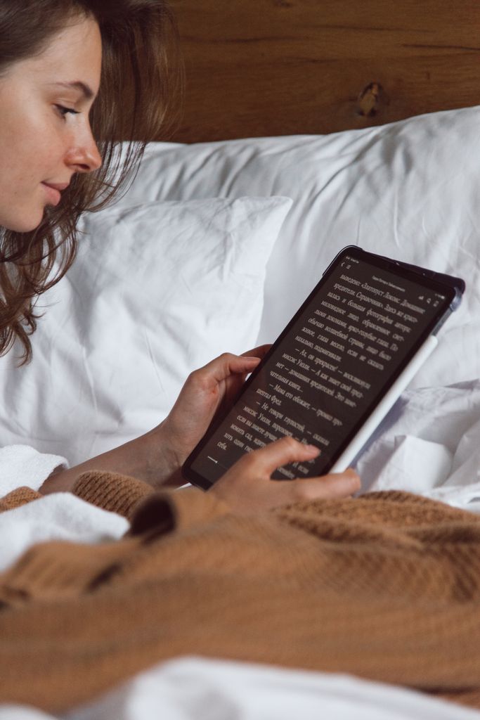 A woman reading on her tablet while lying in bed, creating a cozy and relaxed atmosphere.