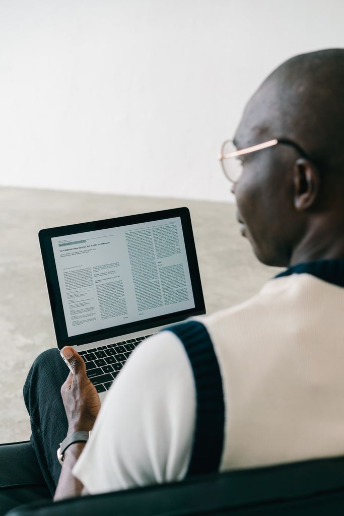 Rear view of an African American man using a laptop indoors with focus on screen content.